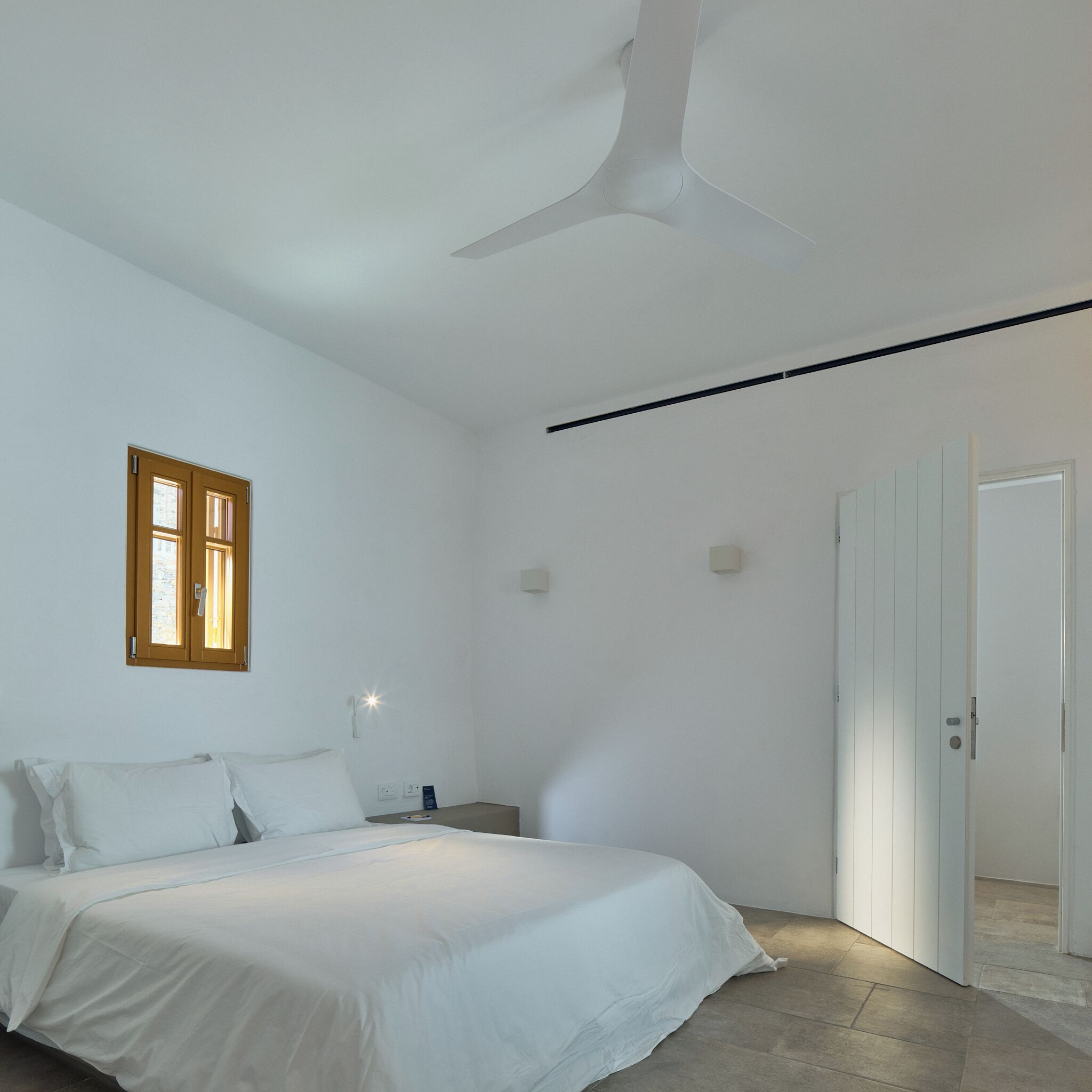Un dormitorio con una cama, una ventana, una puerta y un ventilador de techo.