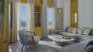 A modern living room with a sofa, armchair, and coffee table, large windows with curtains, and a ceiling fan. - Amorgina (Amorgos)