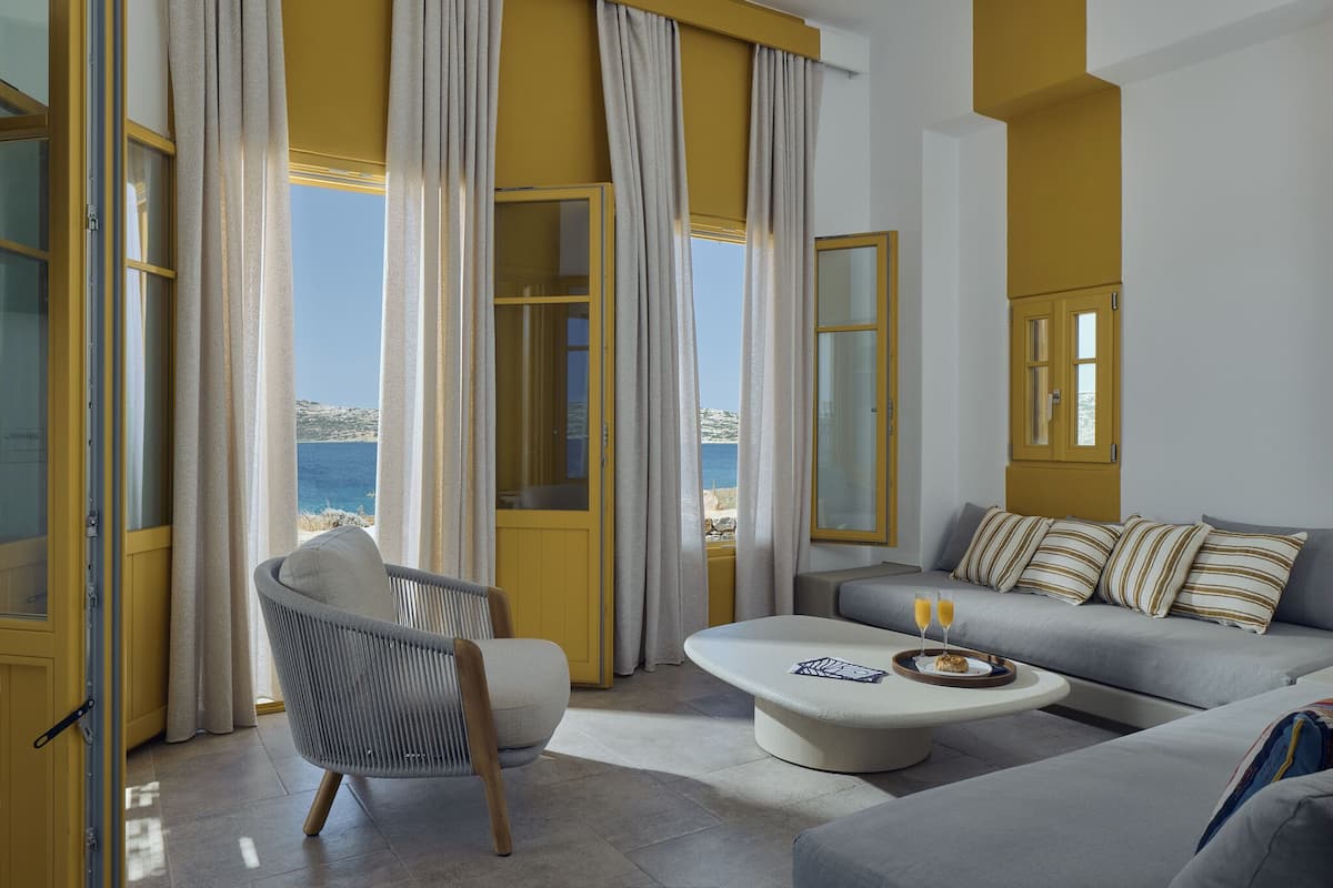 A modern living room with a sofa, armchair, and coffee table, large windows with curtains, and a ceiling fan.