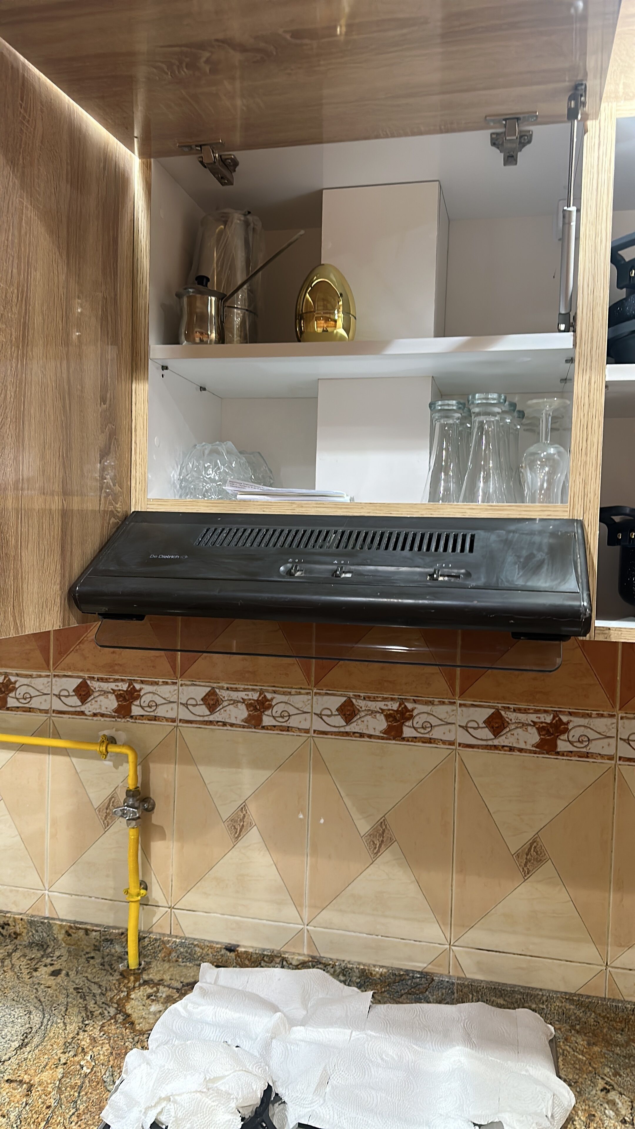 Une cuisine avec une hotte noire, un tuyau jaune et un pare-feu en carreaux.