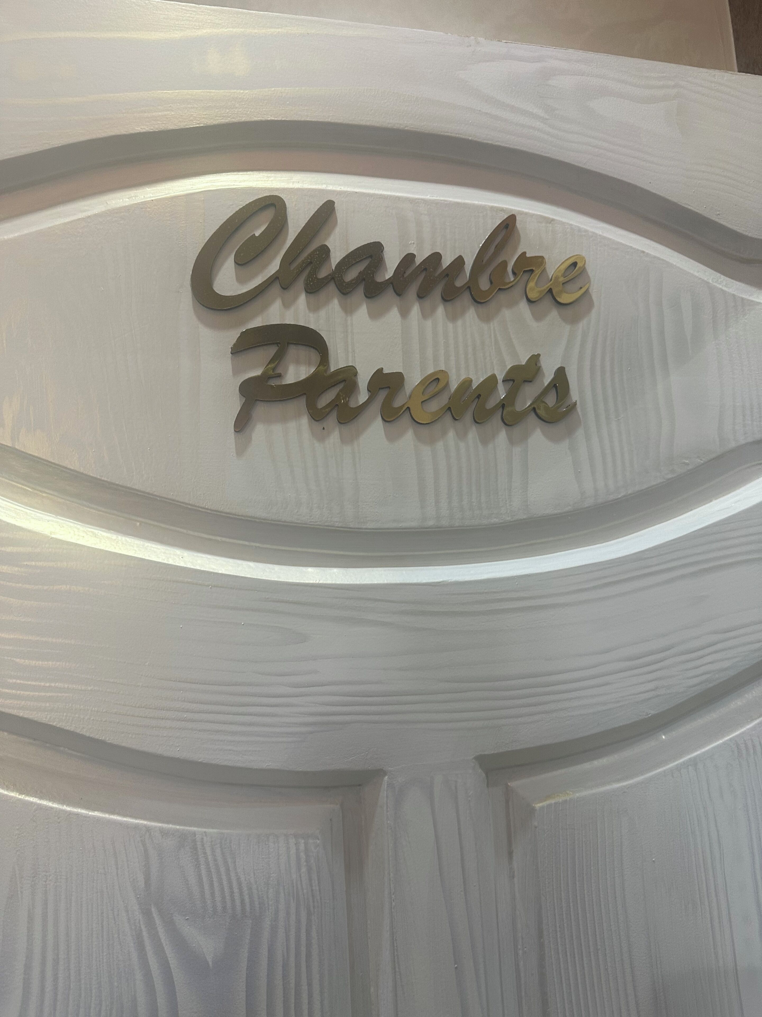 Une porte blanche ornée d’une plaque métallique décorative sur laquelle on peut lire : « Chambre des parents ».