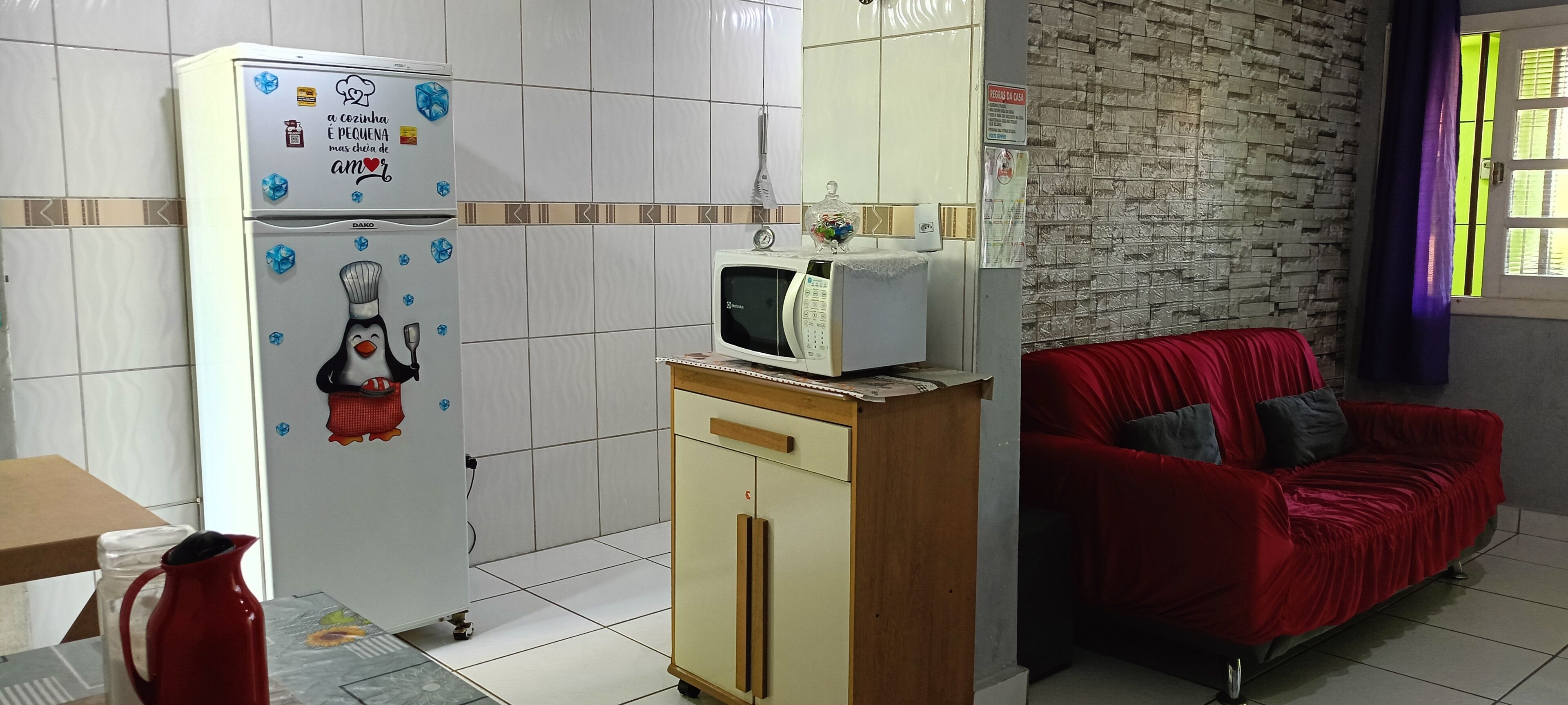 A kitchen with a refrigerator, microwave, and a red sofa.