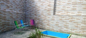 A small outdoor area with a brick wall, a blue pool, and two colorful chairs. - Cozy Grandma's Little House - 200m from the Sea + Pool + Pet-Friendly (Itanhaém)