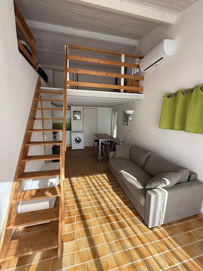 Ein Loft-Zimmer mit Holzleiter, einer Couch, einer Waschmaschine und einem Heizkörper.