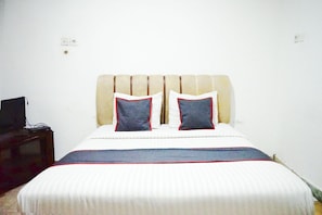 A bed with a striped bedspread, two pillows, and a television on a stand.