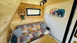 A cozy wooden cabin interior with a patchwork sofa, a window, and a wall-mounted picture of animals.