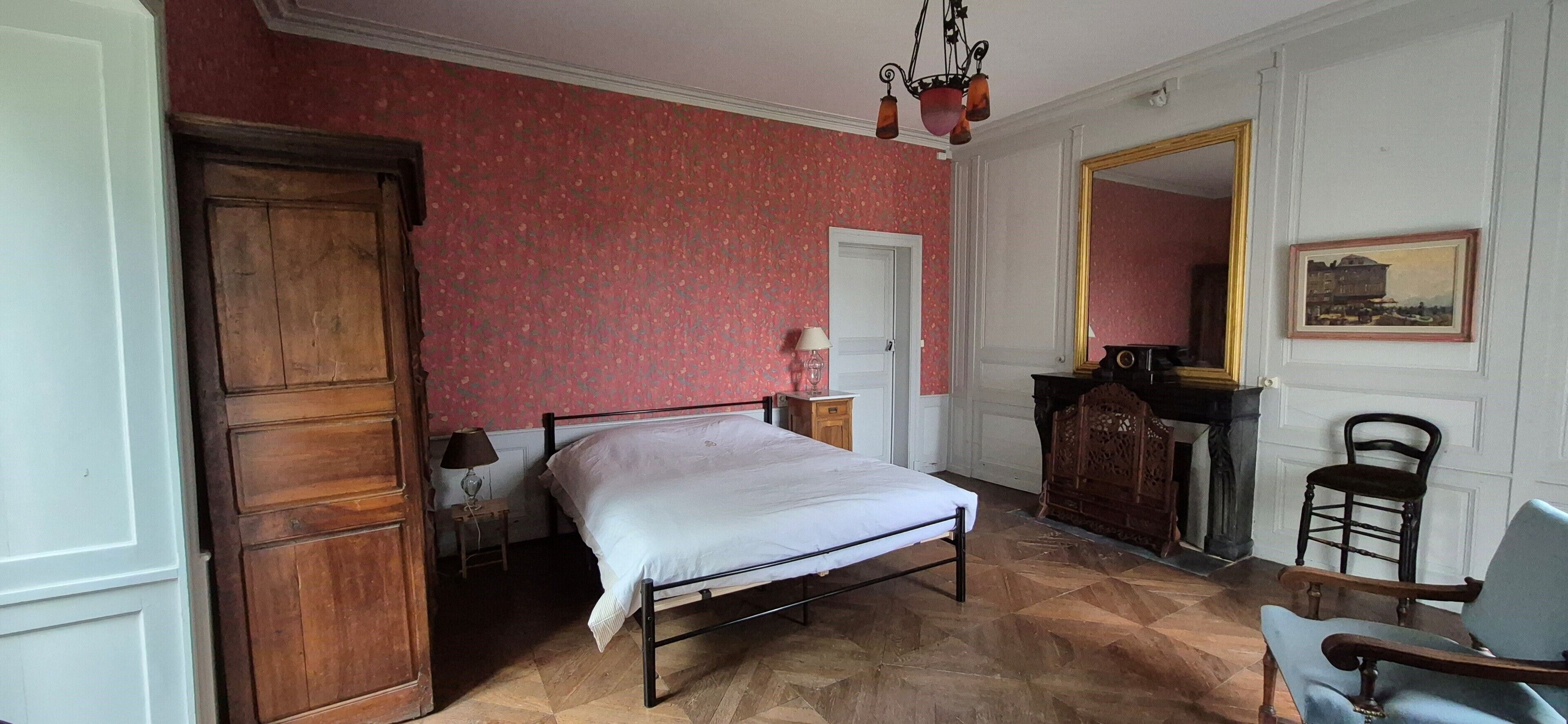 A bedroom with a bed, a wooden wardrobe, a chair, a desk, and a mirror.