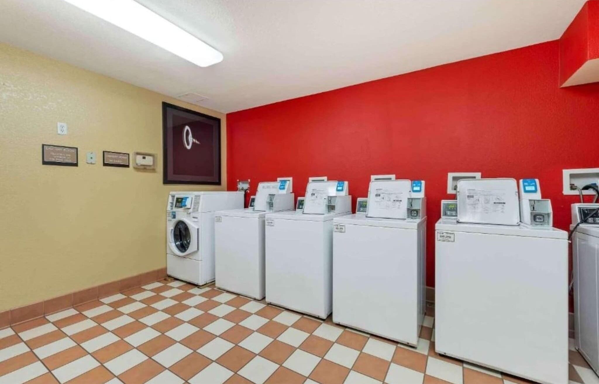 A laundry room with four washing machines, a red wall, and a tiled floor.