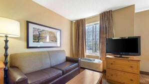 Una camera d'albergo con divano, televisore, un tavolino, un quadro incorniciato e una finestra con tende.