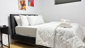 A bedroom with a bed, pillows, a bedside table, a lamp, and artwork on the wall. - Luxury 1 BedRoom Suite | New | Quite | Private| Near Amenities.  (Moncton)