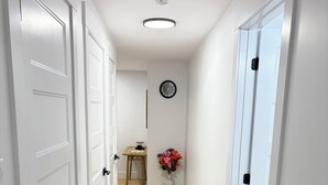 A hallway with white doors, a wooden floor, a wall clock, and a small table with a vase of flowers. - Luxury 1 BedRoom Suite | New | Quite | Private| Near Amenities.  (Moncton)