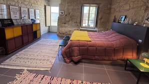 Une chambre avec un grand lit, un mur en pierre, une fenêtre et un bureau avec une chaise.