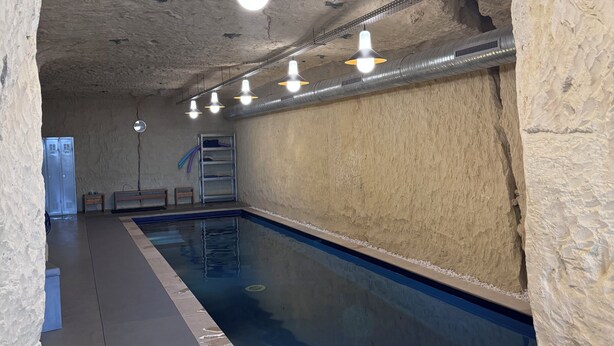 Une piscine intérieure aux murs en pierre, au sol carrelé et dotée de plusieurs luminaires suspendus.