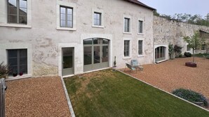 Un bâtiment à deux étages, doté d’une façade en pierre, de nombreuses fenêtres et d’une petite pelouse aménagée avec des sièges.