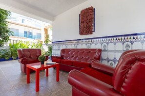 En rød lædersofa med tilhørende lænestol og et lille bord, et dekorativt vægophæng og et flisebeklædt backsplash med et geometrisk mønster.