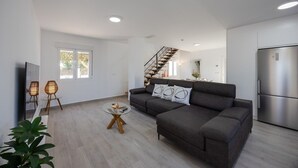 Una sala de estar moderna con un sofá modular, una mesa de centro de vidrio y una escalera que lleva a un nivel superior.