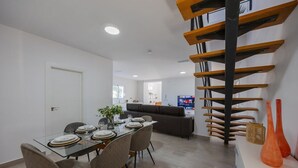 Un comedor con una mesa de vidrio preparada para seis personas, un sofá gris y una escalera de madera.