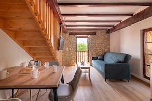 Ein gemütliches Zimmer mit einer Holztreppe, einer Steinwand, einem blauen Sofa und einem Esstisch mit Stühlen.
