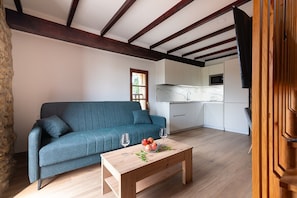 Ein modernes Wohnzimmer mit einem petrolfarbenen Sofa, einem Couchtisch mit Obst und Gläsern sowie einer Küche im Hintergrund.