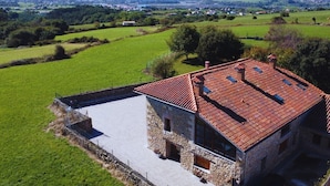A stone building with a red-tiled roof, surrounded by green fields and distant mountains. - Infinity Coast VI by Fidalsa (Miengo)