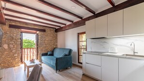 A modern kitchen with white cabinets and a marble countertop, a stone wall, and a blue sofa in a bright room with wooden beams. - Infinity Coast VI by Fidalsa (Miengo)