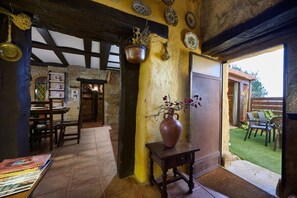 A rustic interior with exposed beams, a dining area with wooden tables and chairs, a large vase with flowers, and a view of the garden outside. - Historichaven by Fidalsa (Labastida)