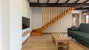 Una sala de estar moderna con una escalera de madera, un televisor de pantalla plana montado en la pared, un sofá verde y una mesa de centro de madera.