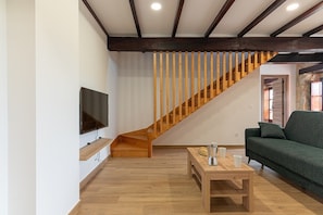 A modern living room with a wooden staircase, a flat-screen TV mounted on the wall, a green sofa, and a wooden coffee table. - Infinity Coast V by Fidalsa (Miengo)