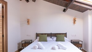 Una cama bien hecha con sábanas blancas y almohadas verdes, dos mesitas de noche con estructura de madera y un techo de madera con vigas a la vista.