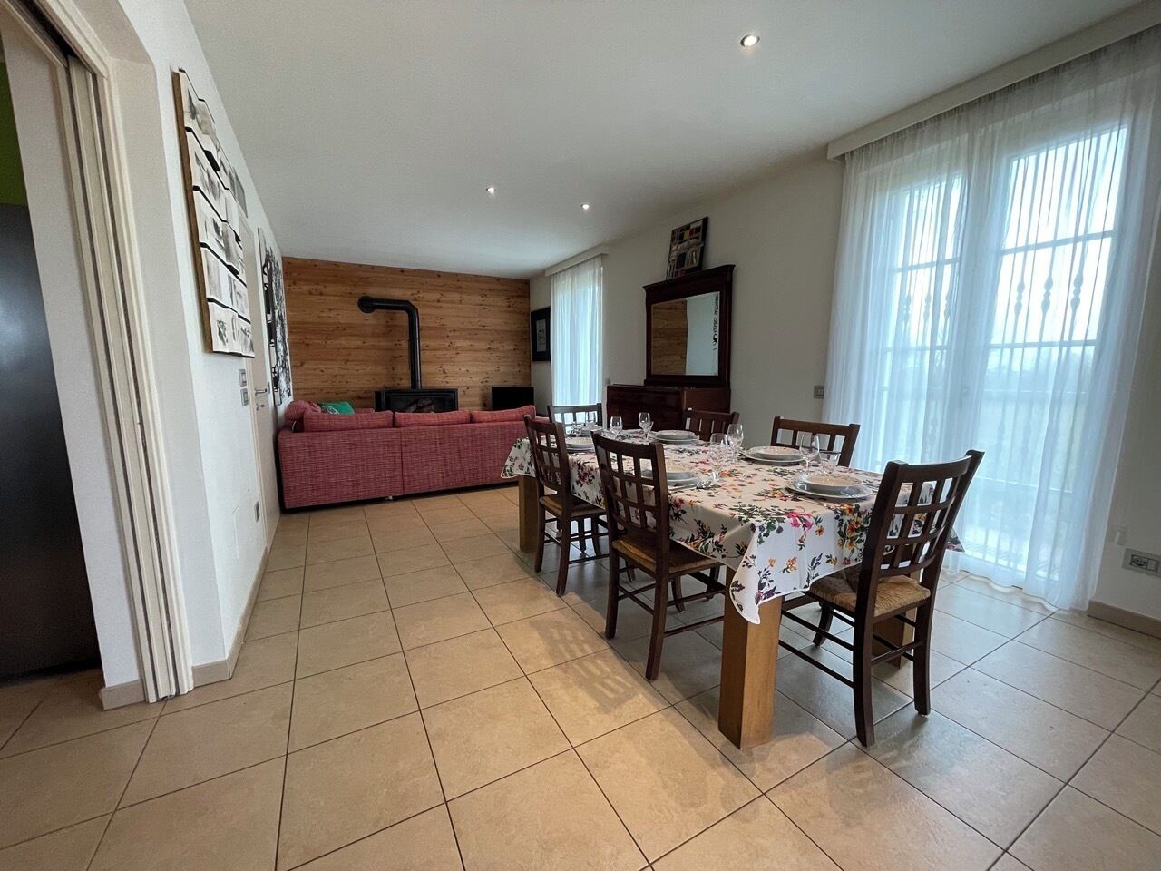 A dining area with a table set for four, a wooden wall, and a sofa in the background.