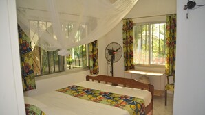 A bedroom with a bed, a desk, a chair, a fan, and a window with curtains. - Vokundahouse Gambia: Your private home away from home (Serekunda)