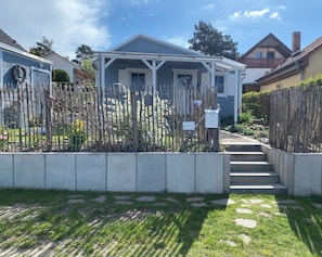 Ein Wohnhaus mit überdachter Veranda, einer Betonmauer zur Stützung und einem Steinweg, der zum Eingang führt.