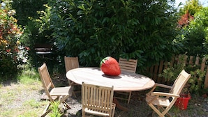 Ein runder Holztisch mit vier Holzstühlen, eine große Erdbeere und ein Holzzaun in einem Garten.