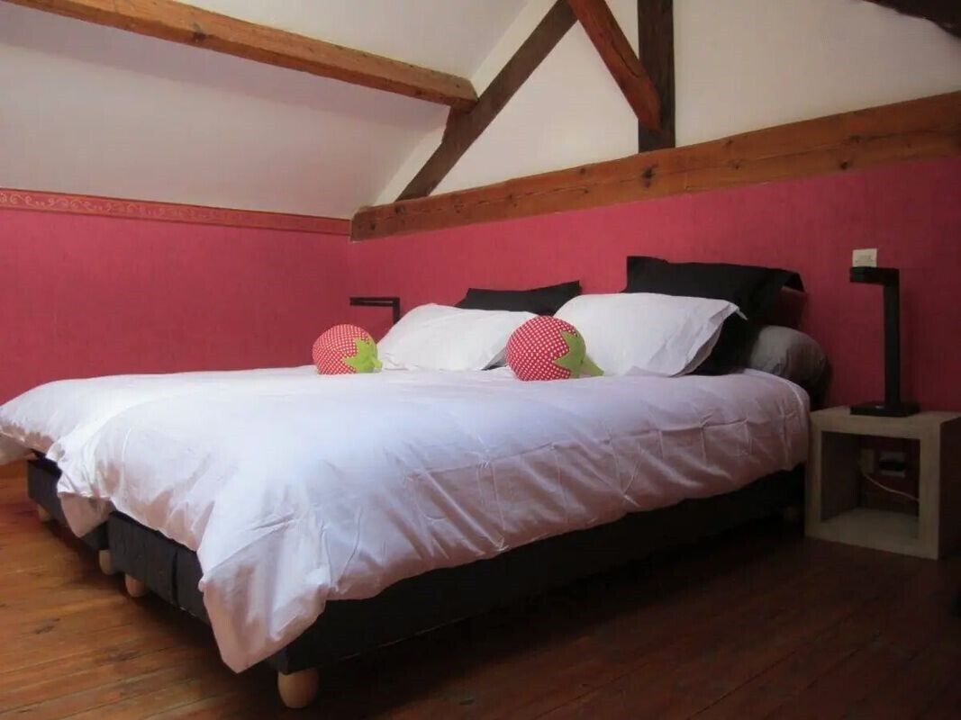Quarto com cama, vigas de madeira, parede rosa e mesa de cabeceira.