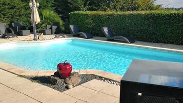 Uma piscina com espreguiçadeiras, uma mesa e uma maçã vermelha na borda.