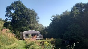 Una petita cabana amb terrassa, envoltada d'arbres densos i un estany.