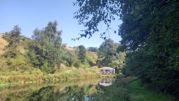 Una cabana amb terrassa al costat d'un llac, envoltada de vegetació densa i arbres.