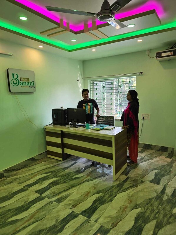 A reception desk with a computer, a sign for 'Hotel Banani,' and a window with bars. - Rajmata Guest House (Krishnanagar)