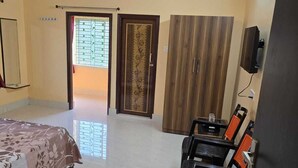 Une chambre à coucher comprenant un lit, un bureau, une chaise, une armoire, un ventilateur de plafond et une porte avec une fenêtre.