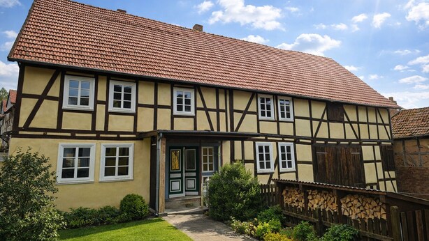 Ett traditionellt hus med korsvirkesfasad, ett tak täckt med tegelpannor, en ytterdörr och en liten trädgård.