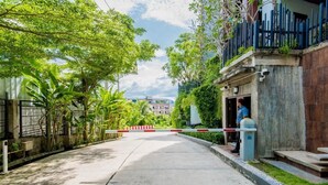 A gated residential area with a concrete pathway, greenery, and a building with a balcony. - Quiet condo with pool vibe (Tambon Patong)
