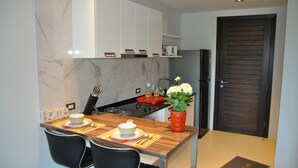 A modern kitchen with white cabinets, a black countertop, and a red vase with flowers. - Quiet condo with pool vibe (Tambon Patong)