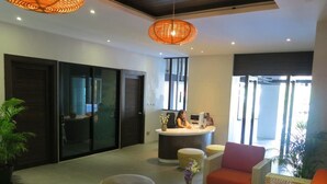 A modern lobby with a reception desk, wicker furniture, and a glass coffee table. - Quiet condo with pool vibe (Tambon Patong)