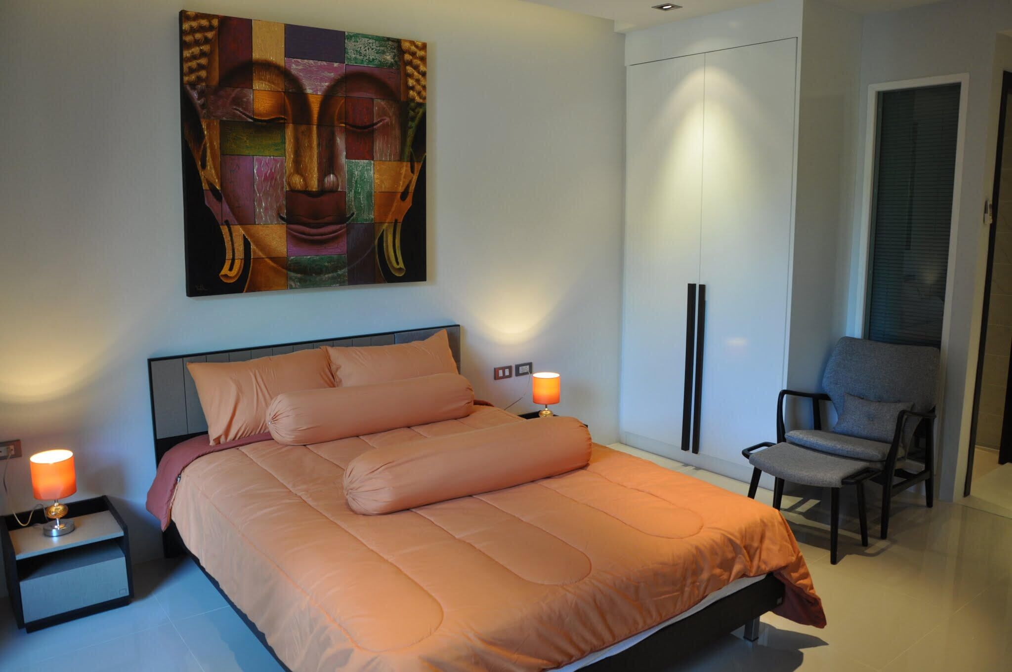 A bedroom with a bed, bedside lamps, a chair, a wardrobe, and a painting on the wall.