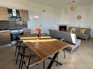 A modern kitchen with a stove, oven, and a wooden dining table with chairs. - Altamira II · 10 Guests · Veranda & Sea Views (Zakynthos)