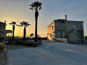 A building with a balcony, a staircase, and a parking area with palm trees. - Altamira II · 10 Guests · Veranda & Sea Views (Zakynthos)