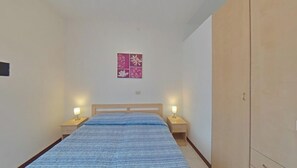 A bedroom with a bed, two bedside tables, a nightstand, a wardrobe, and a wall-mounted floral artwork. - Convenient flat in a great location (Lignano Sabbiadoro)