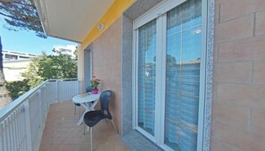 A balcony with a table and chairs, a potted plant, and a window with a view of buildings. - Convenient flat in a great location (Lignano Sabbiadoro)