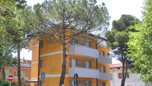 A multi-story building with balconies, a tree in front, and parked cars. - Flat steps from the sea and center (Lignano Sabbiadoro)