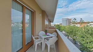 Ein Balkon mit Tisch und Stühlen, einem Blumentopf und Blick auf Gebäude und Grünflächen.